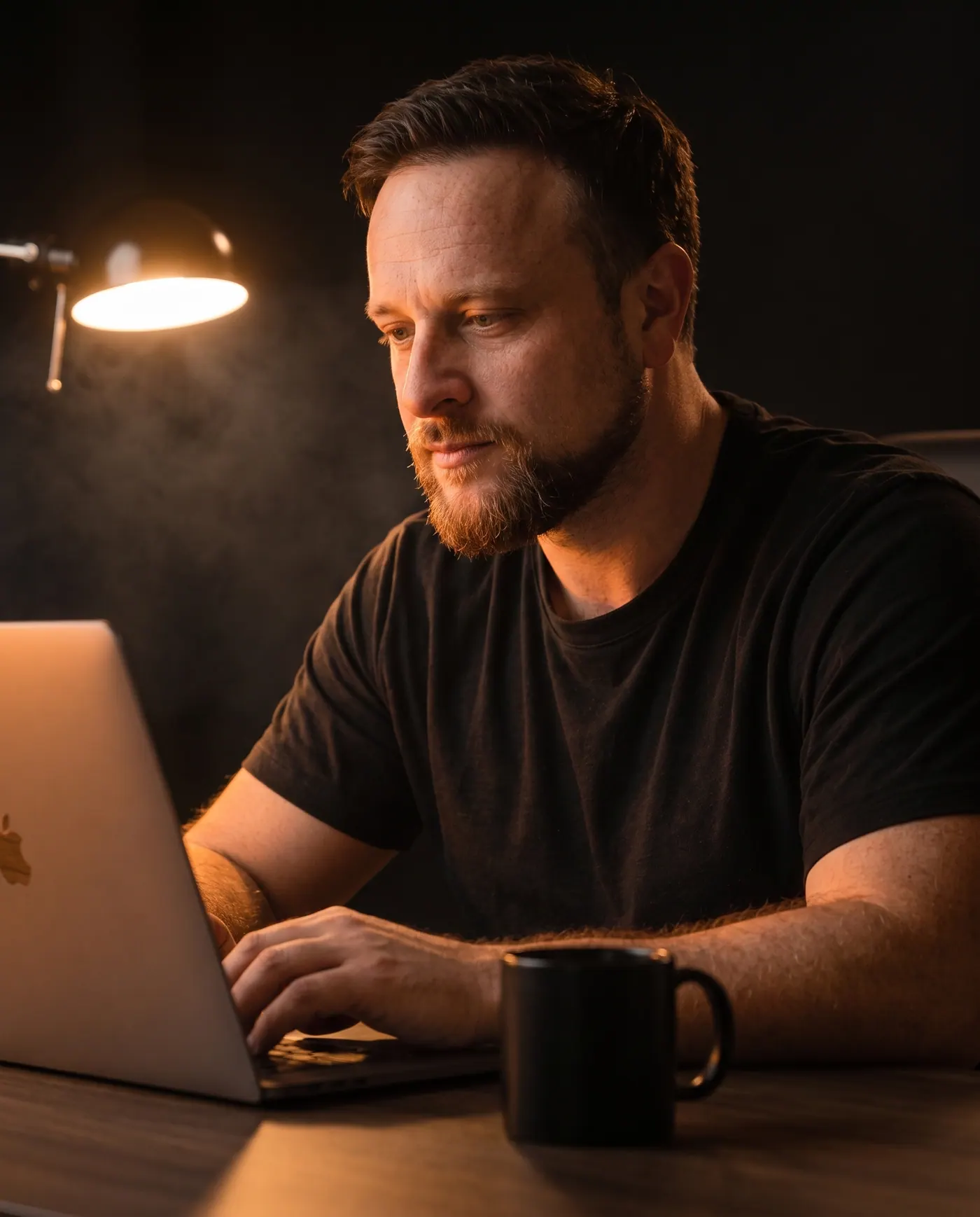 Erol Orahovac sitzt im dunklen Studio am Schreibtisch und arbeitet konzentriert am Laptop, hinter ihm leuchtet eine Schreibtischlampe.